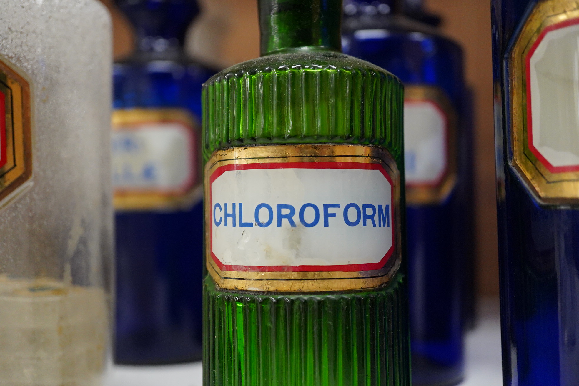 Seventeen 19th/early 20th century glass apothecary jars with gilt rimmed labels; six blue glass, ten clear glass and a green glass example, labels including; Syr: Zingib:, Chloroform, Syr: Rhei:, Camphora, etc. tallest 2